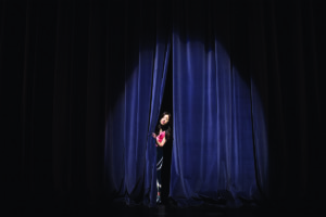Introvert peeking out from behind a curtain on stage
