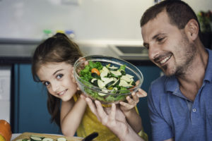 Dad helping young daughter eat more vegetables