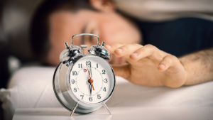 Person in bed hitting snooze and not getting sleep