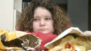 Teen with junk food appearing dejected from weight stigma