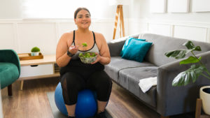 Woman with healthy diet and exercise habits sitting on a ball and eating a salad