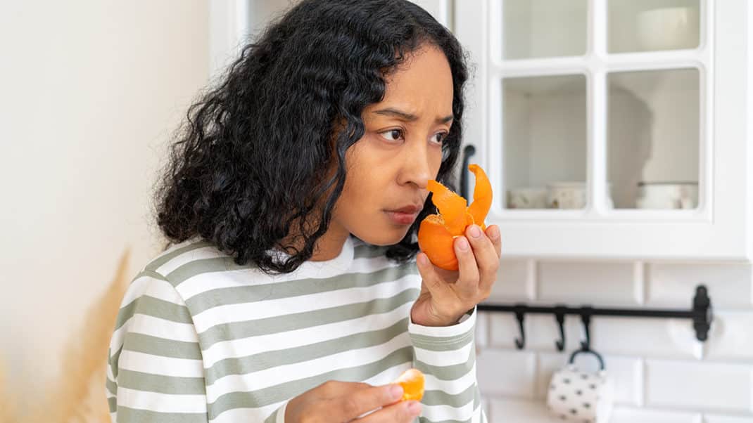 Woman smelling orange peel to show loss of taste and smell from COVID