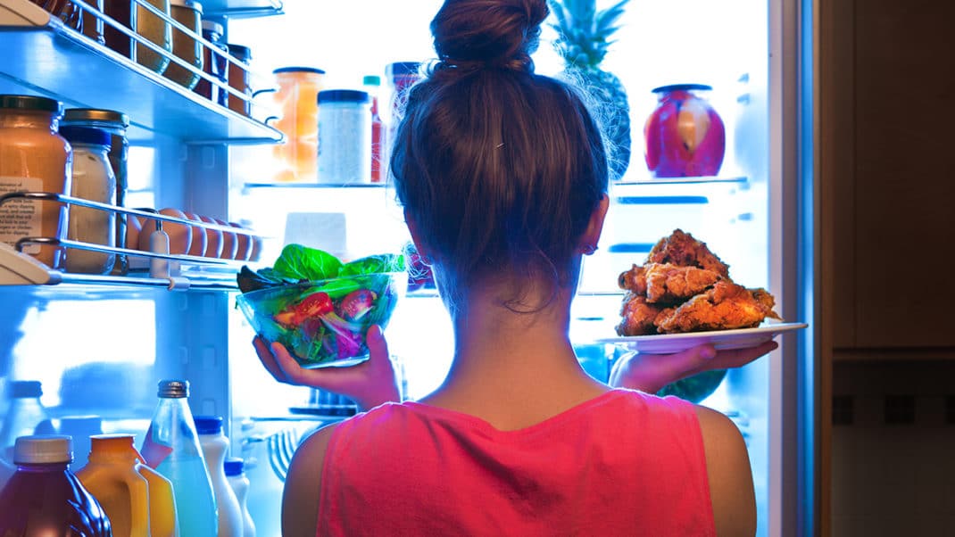 Girl standing in front of the fridge weighing food options for healthy eating