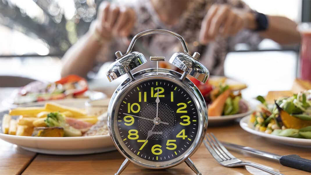 A clock in front of someone eating to represent intermittent fasting