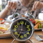 A clock in front of someone eating to represent intermittent fasting