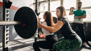 Trainer helping woman lift weights to show DOMs