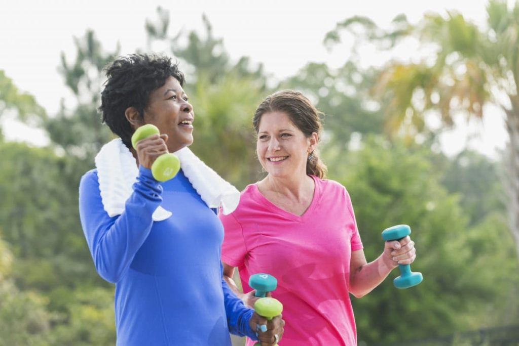 Two women improving their cardiovascular fitness by walking briskly with hand weights.