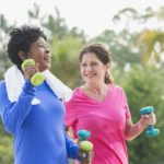 Two women improving their cardiovascular fitness by walking briskly with hand weights.